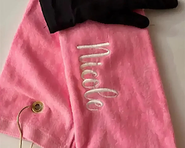 Personalized pink golf towel with embroidered name and black golf glove on white background