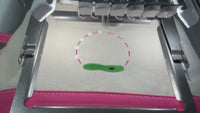 8 second video of embroidery machine stitching a small pouch with a golf frame. Bag is canvas with hot pink on the bottom. 
