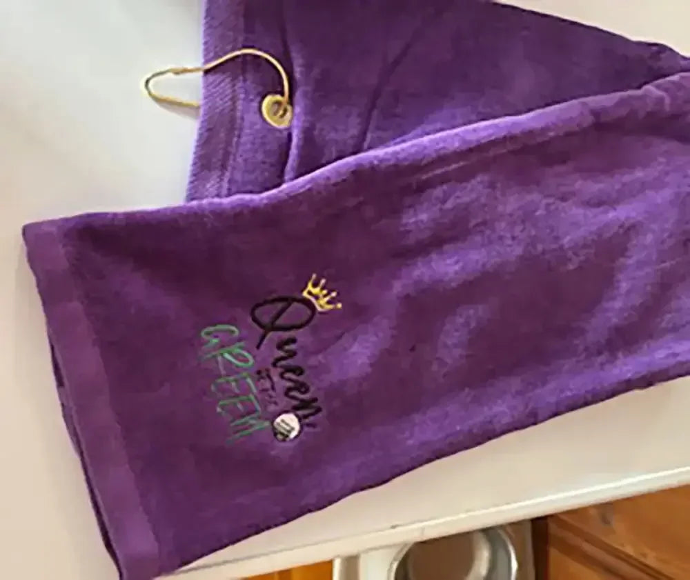 Purple embroidered golf towel with 'Queen of the Green' and crown design, gold clip attached