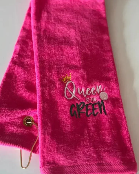 Bright pink embroidered golf towel with 'Queen of the Green' text and a gold grommet