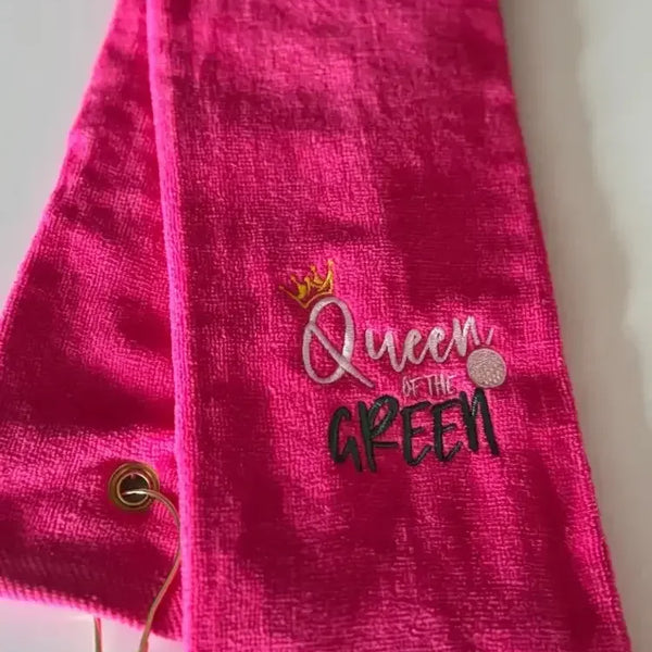 Bright pink embroidered golf towel with 'Queen of the Green' text and a gold grommet
