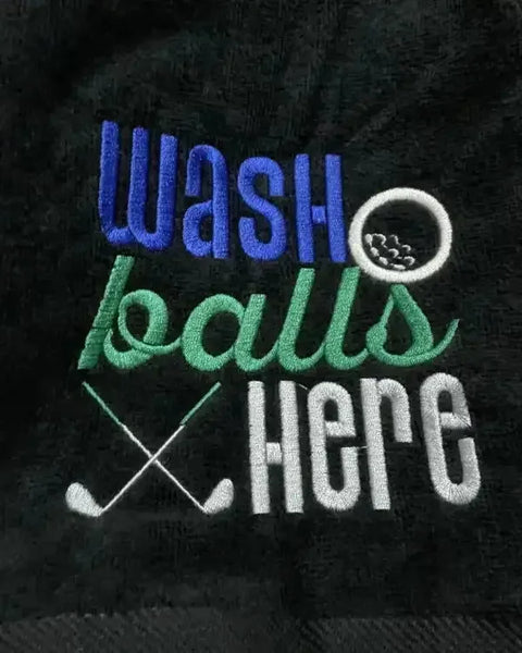 Black embroidered golf towel with 'wash balls here' text, golf ball, and crossed clubs design