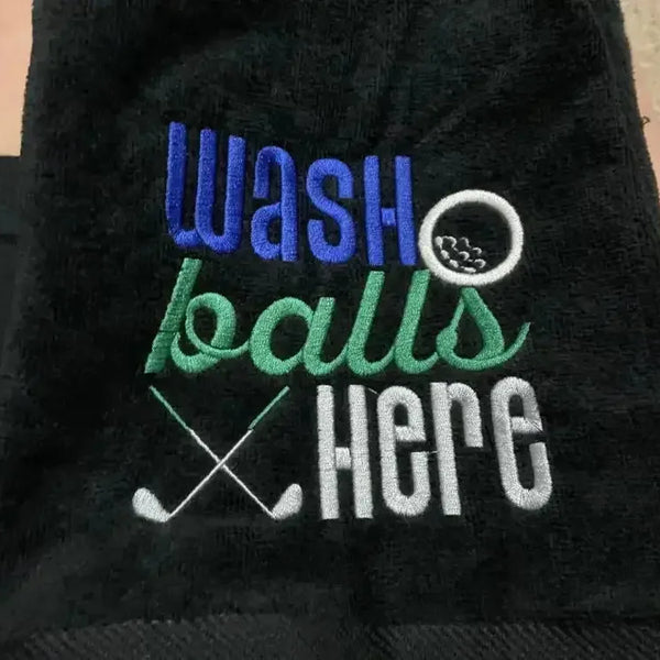 Black embroidered golf towel with 'wash balls here' text, golf ball, and crossed clubs design