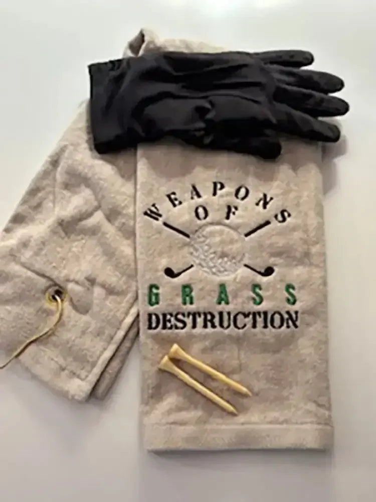 Embroidered golf towel reading 'Weapons of Grass Destruction' with golf gloves and tees