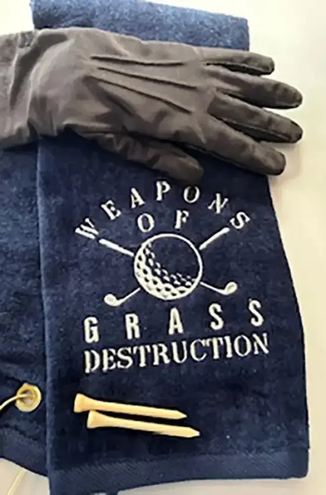 Navy embroidered golf towel with 'Weapons of Grass Destruction' design, golf glove, and tees