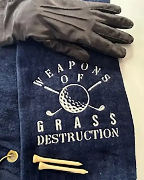Navy embroidered golf towel with 'Weapons of Grass Destruction' design, golf glove, and tees
