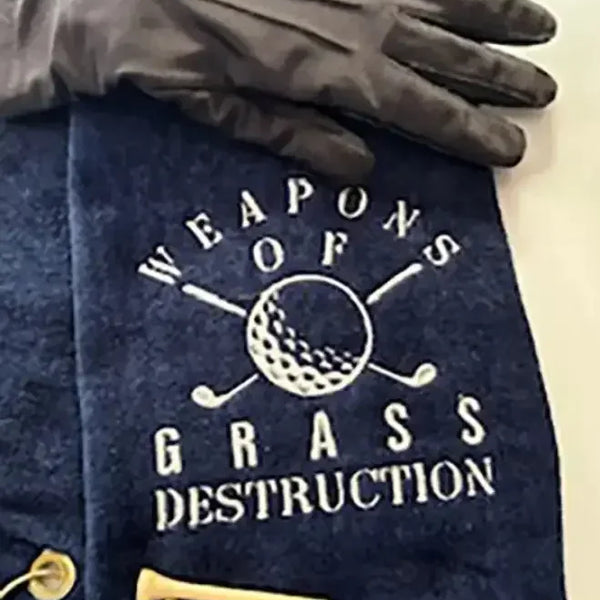 Navy embroidered golf towel with 'Weapons of Grass Destruction' design, golf glove, and tees