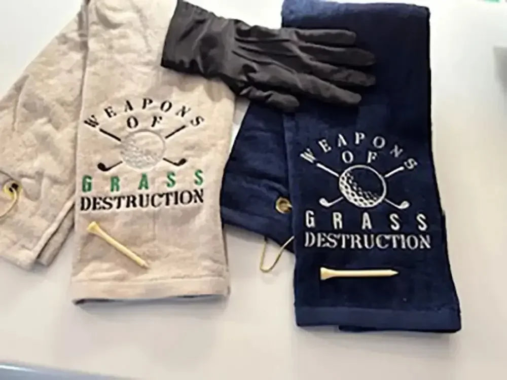 Embroidered golf towels with 'Weapons of Grass Destruction' text, golf tees, and glove.