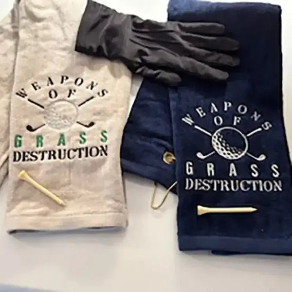 Embroidered golf towels with 'Weapons of Grass Destruction' text, golf tees, and glove.