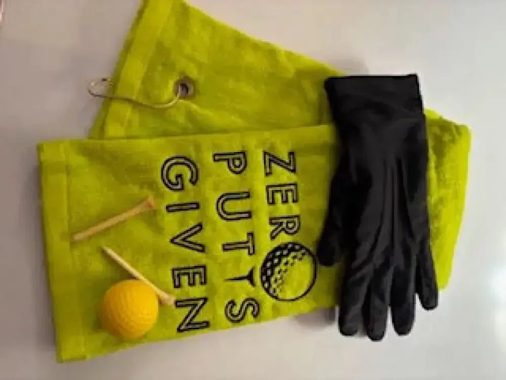 Yellow embroidered golf towel with 'Zero Putts Given' text, golf glove, tees, and ball