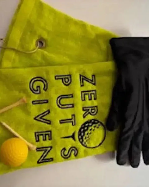 Yellow embroidered golf towel with 'Zero Putts Given' text, golf glove, tees, and ball